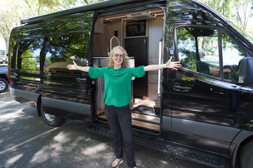 A woman stands beside a black van with its doors open, ready for an adventure.